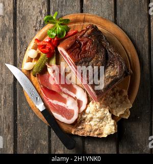 Bacon tyrolien sur une carte Schüttelbrot (pain croustillant sans levain du Tyrol du Sud) avec des conichons, de la laitue d'agneau et un couteau Banque D'Images