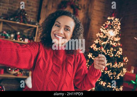 Photo d'adorable jeune femme adorable vêtue rouge pull-over appréciant l'enregistrement de noël auto-vidéo tenant des ampoules à l'intérieur de la maison de pièce Banque D'Images