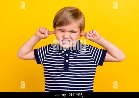 Photo portrait petit garçon portant des vêtements décontractés oreilles fermées avec les doigts isolé couleur jaune vif fond Banque D'Images