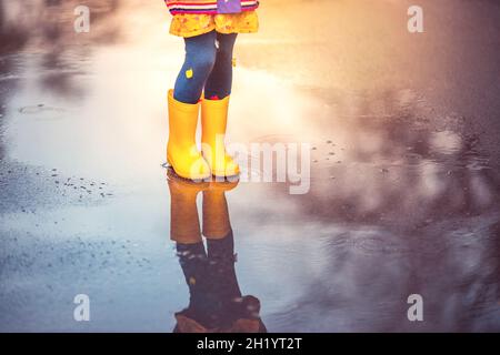 Pieds d'enfant dans des bottes en caoutchouc coloré sautant par-dessus la flaque sous la pluie.Parc d'automne. Banque D'Images