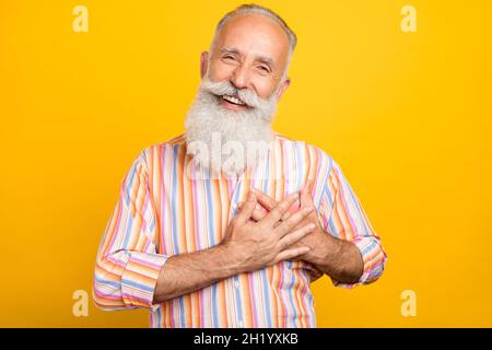 Photo de positif heureux heureux reconnaissant les mains de pensionné coeur porter chemise rayée isolé couleur jaune fond Banque D'Images