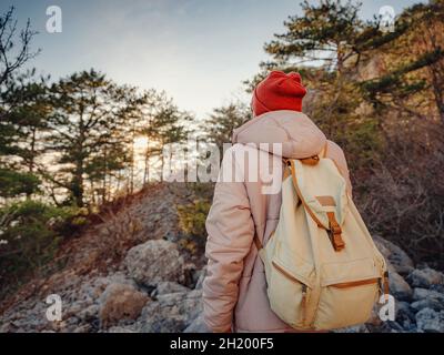 homme avec sac à dos et chapeau rouge randonnée dans les montagnes au coucher du soleil se dresse sur le sentier de randonnée ou chemin rocheux.Temps froid.Randonnée en hiver.Vibes et aventures en plein air Banque D'Images