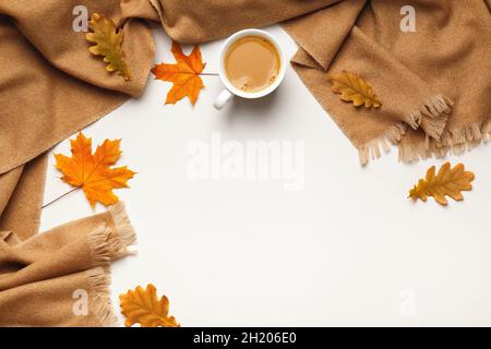 Concept de coziness automne hiver.Tasse à café avec foulard beige en cachemire et feuilles d'érable et chêne déchue sur fond blanc.Espace de copie de la vue de dessus de la pose à plat Banque D'Images