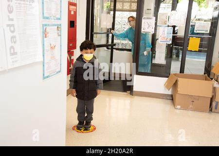 Éducation préscolaire garçon de 4-5 ans attendant son tour sur le marqueur de plancher au début de la journée, membre du personnel en robe regardant pour voir que l'enseignant vient à Banque D'Images