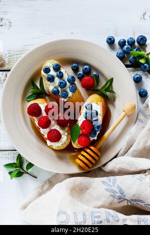 Assiette en céramique blanche de sandwiches doux au dessert avec baies fraîches, myrtille et framboise, fromage à la crème, menthe et miel Banque D'Images