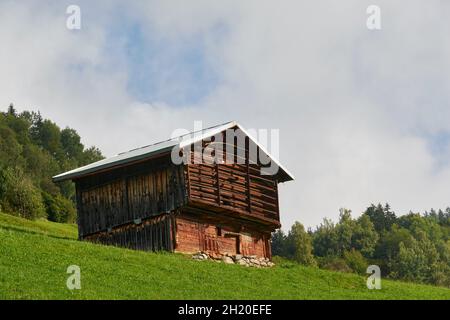 Hay Barn dans le style architectural typique de Surselva sur le pré alpin.En arrière-plan Une forêt de Fir et Un ciel légèrement nuageux.Surselva Grisons SWI Banque D'Images