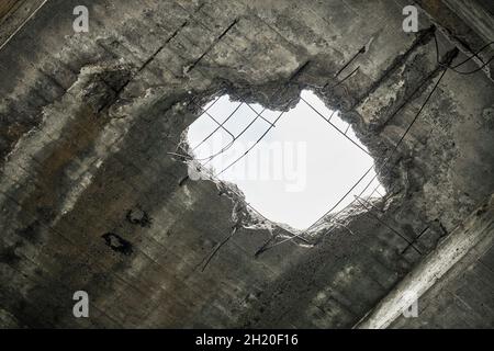 Ancien toit de maison endommagé abandonné avec trou dans le plafond donnant sur ciel nuageux.Mur de béton écroulé avec trou dans un bâtiment industriel abandonné, Banque D'Images