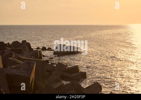 Vue sur la mer avec de grands brise-lames en béton au beau coucher de soleil orange, les vagues de mer se brisent dans les brise-lames faites de rochers au soleil du soir.À quelques centaines de mètres Banque D'Images