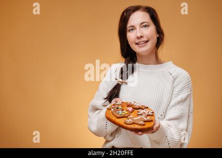 Femme boulangère en chandail blanc tient un plateau avec des biscuits épicés. Banque D'Images