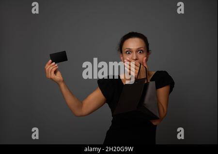 Une femme africaine surprise tient une carte noire de crédit ou de réduction d'une main et couvre sa bouche d'une autre main, surprise par les ventes du Vendredi fou.SHO Banque D'Images
