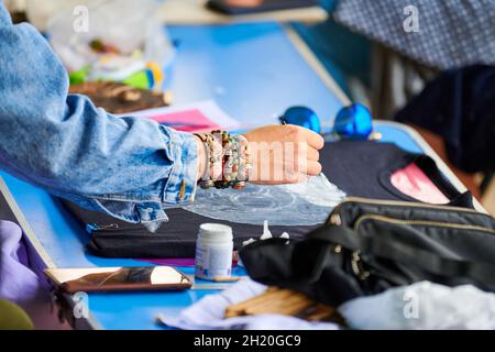 Femme artiste peinture à la main sur T-shirt noir à l'aide de la peinture à la brosse et à la toile, atelier à l'extérieur.Créez votre propre atelier de t-shirt, relooking for unique A. Banque D'Images