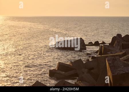 Vue sur la mer avec de grands brise-lames en béton au beau coucher de soleil orange, les vagues de mer se brisent dans les brise-lames faites de rochers au soleil du soir.À quelques centaines de mètres Banque D'Images