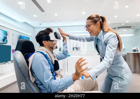 Couple multiculturel heureux essayant la technologie de réalité virtuelle. Intérieur du magasin du technicien. Banque D'Images