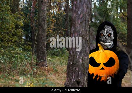 Grim reaper tenant la tête de citrouille d'halloween.Homme dans le masque de la mort wi Banque D'Images