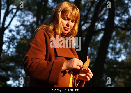 Portrait d'une femme blonde de race blanche d'âge moyen dans le parc d'automne.Femme lumineuse et élégante en manteau orange et châle de cou marchant dans le parc d'octobre.Triste automne Banque D'Images