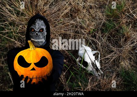 Gros plan de la couche sinistre.Homme dans le masque de la mort avec une flamme de feu dans les yeux sur l'herbe sombre et sèche avec le fond du crâne animal.Costume de carnaval, créepy Banque D'Images