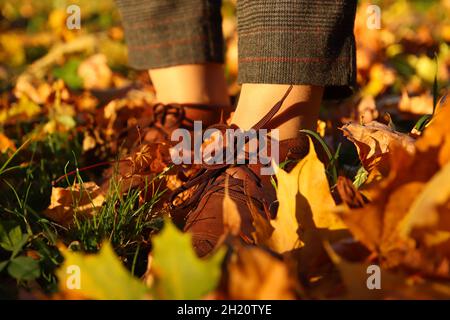 Pied féminin en gros plan avec pantalon capri et chaussures à brogues sur fond de feuilles brillantes et sèches d'automne.Femme brillante et élégante en manteau orange marchant en octobre Banque D'Images