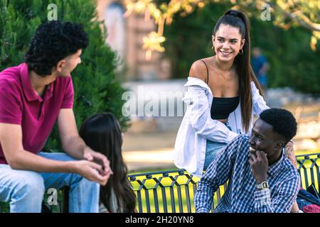 Jeunes de différentes origines ethniques assis sur un banc et parlant Banque D'Images