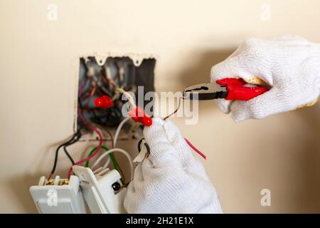 Un électricien remplace un interrupteur mural.Un concept de projet DIY.Danger de haute tension. Porter des gants en caoutchouc pour la protection.Le professionnel est maki Banque D'Images
