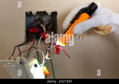 Un électricien remplace un interrupteur mural.Un concept de projet DIY.Danger de haute tension.Un testeur de tension sans contact et des gants de protection en caoutchouc sont utilisés Banque D'Images