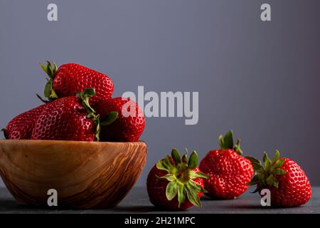 Gros plan image isolée d'un bol en bois rempli de fraises fraîches crues sur fond de pierre sombre.Riche en nutriments, nourriture biologique brute pour lui Banque D'Images