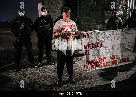 Cracovie, Pologne, 18/10/2021, Un manifestant portant un t-shirt avec un emblème national polonais, un barbelé sur ses mains et tenant une bougie vue à côté d'un groupe de policiers garant la porte du château, lors d'une manifestation contre les visites.En 2010, le président polonais Lech Kaczynski est décédé dans un accident d’avion avec plus d’une centaine de délégués, principalement des responsables d’État importants.Depuis, son frère jumeau, Jaroslaw Kaczynski, vice-premier ministre actuel et leader de l'arrière-siège de la Pologne, visite chaque mois la tombe de Lech au château de Wawel à Cracovie, accompagnée de l'ensemble du gouvernement polonais.Ceux-ci Banque D'Images