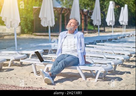 Homme assis sur une chaise longue au soleil Banque D'Images