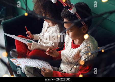 Des enfants afro-américains mignons écrivent des lettres au père Noël chez eux Banque D'Images