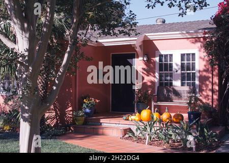 Magnifique cottage rose avec un stoop en terre cuite, contenant une rangée de belles citrouilles orange de différentes tailles. Banque D'Images