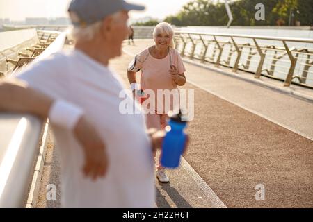 Un homme senior heureux court le long de la passerelle tandis que le gentleman se repose près de la main courante Banque D'Images