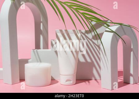 Récipients blancs cosmétiques avec feuille de palmier sur fond rose.Produits de soins pour la peau.Pot de crème hydratante pour les mains, le visage, le corps et tube en plastique Banque D'Images