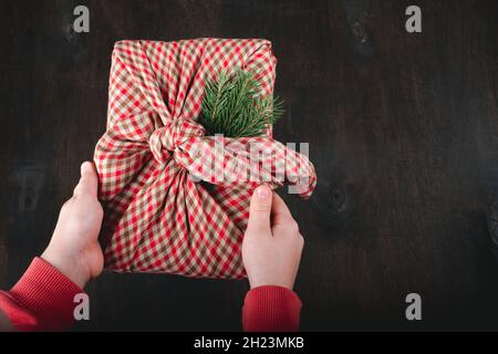Les mains des enfants tenant l'emballage cadeau dans le tissu naturel dans le style de Furoshiki.Des cadeaux durables.Aucun gaspillage.Noël vacances écologiques.Phot de haute qualité Banque D'Images