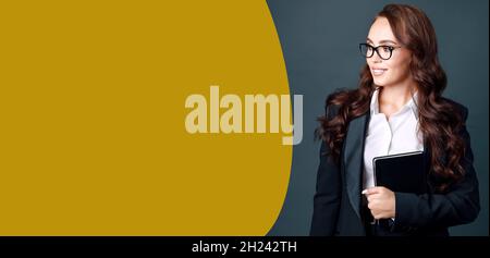 Une belle femme caucasienne en lunettes et un costume d'affaires regarde l'espace vide et sourit.Bannière prête pour l'annonce avec un portrait d'une charmante brunette. Banque D'Images