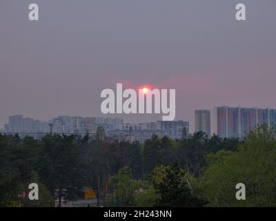 Soirée rouge coucher du soleil brillant à travers le smog violet au-dessus de la ville de Kiev (Kiev) avec des bâtiments à l'horizon.Paysage urbain industriel avec ciel pittoresque. Banque D'Images