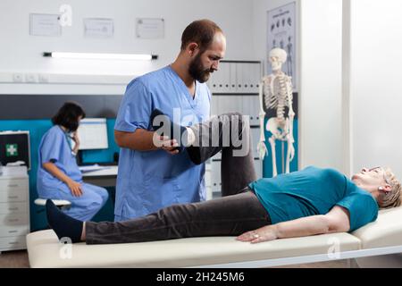 Médecin généraliste aidant la femme à la retraite souffrant de douleurs articulaires pour un examen orthopédique.Médecin faisant de l'exercice chiropratique pour le patient aîné avec des blessures de jambe et de genou, traitant l'arthrite. Banque D'Images