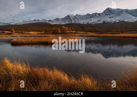 Un incroyable coucher de soleil d'automne sur le lac, une île sur le lac, des montagnes couvertes de neige et de forêt, des mélèzes dorés et des reflets dans l'eau contre Banque D'Images