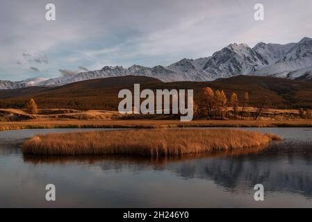 Un incroyable coucher de soleil d'automne sur le lac, une île sur le lac, des montagnes couvertes de neige et de forêt, des mélèzes dorés et des reflets dans l'eau contre Banque D'Images
