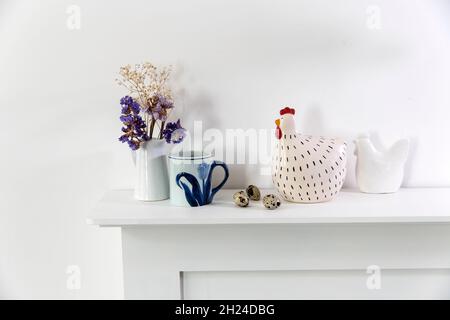 Fleurs bleues séchées dans un vase, deux sculptures en faïence d'un poulet et des œufs de caille décorent la table à la veille de Pâques Banque D'Images