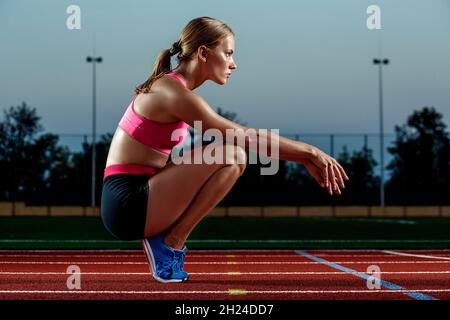 Photo d'une jeune femme européenne ou d'un sprinter assis sur une piste de stade en plein air, se sentant épuisée après un sprint ou un marathon. Banque D'Images