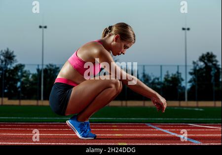 Photo d'une jeune femme européenne ou d'un sprinter assis sur une piste de stade en plein air, se sentant épuisée après un sprint ou un marathon. Banque D'Images