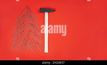Ongles longs et marteau, disposés en forme d'arbre de Noël sur fond rouge.Bannière.Pose à plat.Copier l'espace Banque D'Images