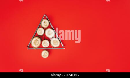 De longs clous et des coupes de bois ou des dalles de branches, disposés en forme d'arbre de Noël sur fond rouge.Bannière.Pose à plat.Copier l'espace Banque D'Images