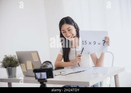 Jeune belle femme enseignante asiatique enseigner les mathématiques en ligne et regarder l'ordinateur portable pour discuter avec l'étudiant devant la caméra pendant la quarantaine et le travail de la maison. Banque D'Images