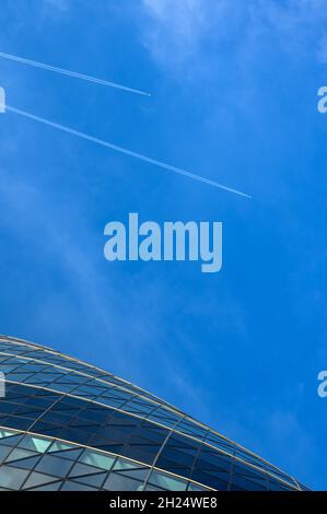 Des avions à haute altitude qui coupent le ciel au-dessus de la Cité de Londres avec des contrailles, ainsi qu'une section du bâtiment Gherkin illustré.Londres, Angleterre. Banque D'Images