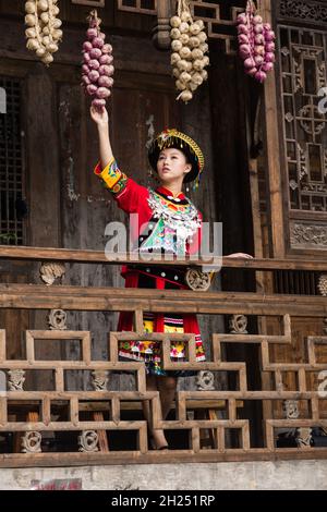 Une jeune femme attirante en robe traditionnelle de Tujia ethnique pose pour un portrait à Furong, en Chine.Des liasses d'oignons de couleur pendent des avant-vêtements comme d Banque D'Images