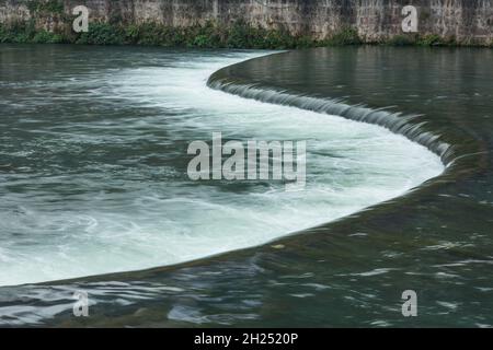 L'eau s'écoule sur un déversoir en forme de S à travers la rivière Tuojiang à Fenghuang, en Chine. Banque D'Images