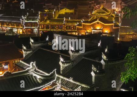 des statues stylisées de phoenix sur les toits de l'ancienne ville de Fenghuang, en Chine, s'illuminent la nuit. Banque D'Images