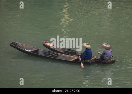 Deux hommes dans un conique traditionnel ont des échantillonages de pagaie sur la rivière Tuojiang à Fenghuang, en Chine. Banque D'Images