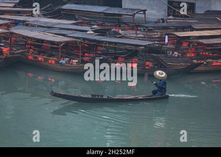 Un homme dans un chapeau conique traditionnel pagaie un sampan sur la rivière Tuojiang à Fenghuang, en Chine. Banque D'Images