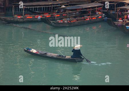 Un homme dans un chapeau conique traditionnel pagaie un sampan sur la rivière Tuojiang à Fenghuang, en Chine. Banque D'Images